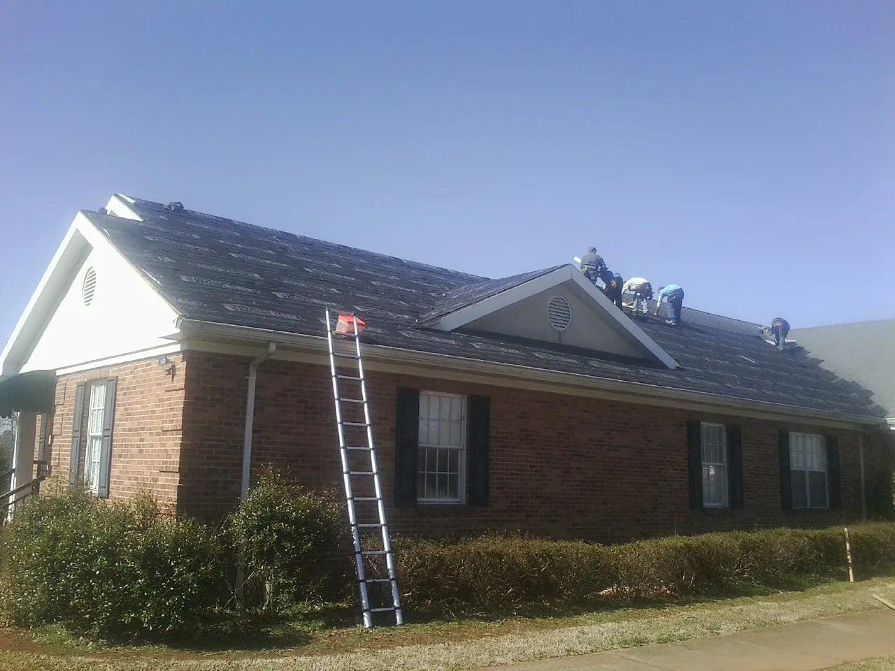 Crew tearing shingles off a brick ranch roof with a ladder set — Metal Roof Repair work by our crew in Encino