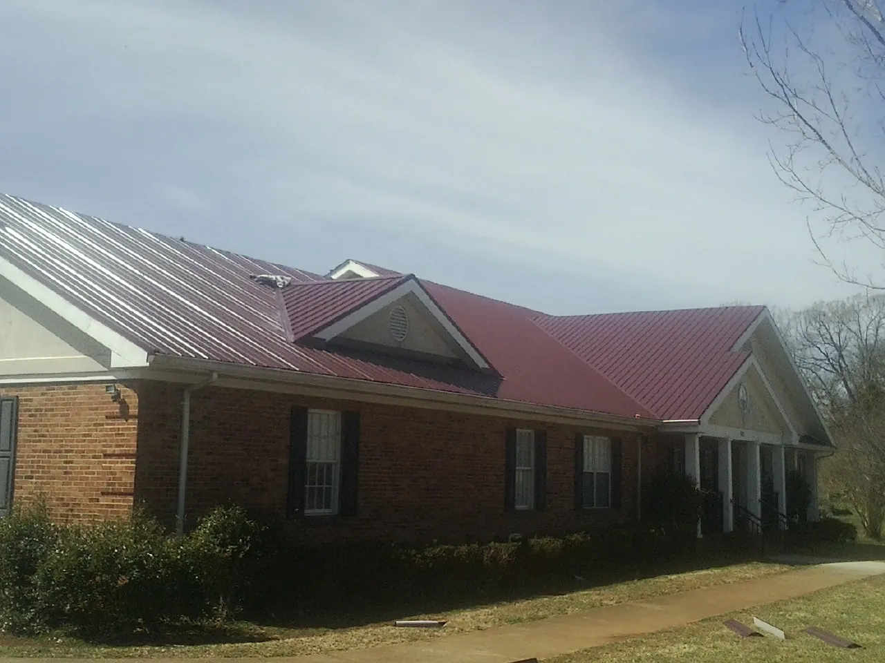Red metal roof with gabled entries on a long brick building, from a Hail Damage Roof Repair job in Encino