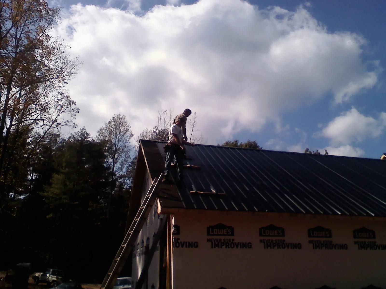 Roofer fastening dark metal panels high against a cloudy sky, from a Roof Inspection job in Encino